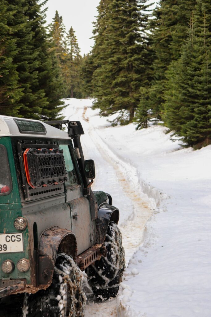 Green Land Rover Defender on a snowy forest trail with recovery boards mounted on its side