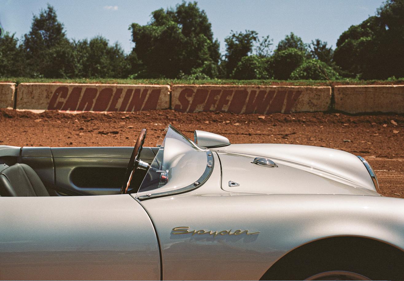 Profile of the Porsche 550 J showing gold Spyder script and wraparound windscreen in front of a Carolina Speedway wall