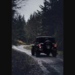 Black off-road SUV driving down a forest gravel trail, representing the rugged Scout Traveler Trail-Ready concept