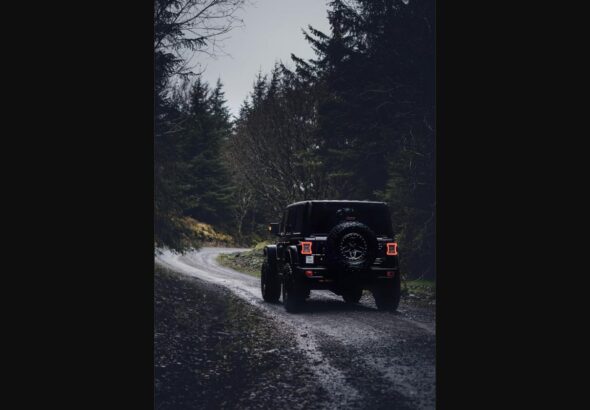 Black off-road SUV driving down a forest gravel trail, representing the rugged Scout Traveler Trail-Ready concept