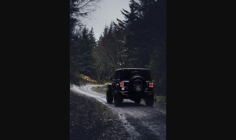 Black off-road SUV driving down a forest gravel trail, representing the rugged Scout Traveler Trail-Ready concept