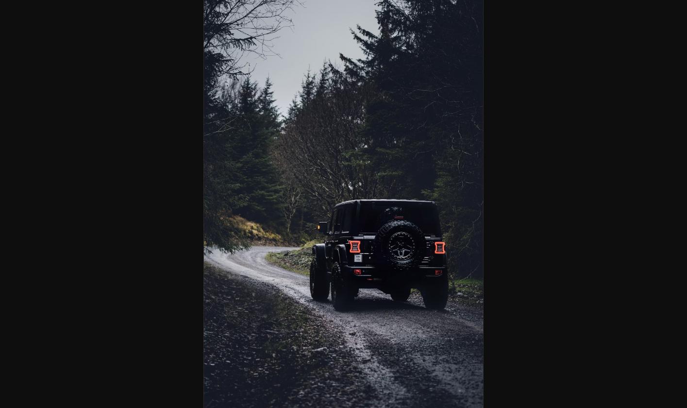 Black off-road SUV driving down a forest gravel trail, representing the rugged Scout Traveler Trail-Ready concept