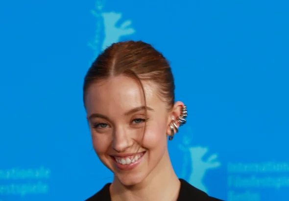 Sydney Sweeney smiling in a black blazer against a blue Berlinale backdrop