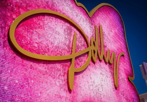 A large pink sequined heart sign with gold cursive lettering against a blue sky