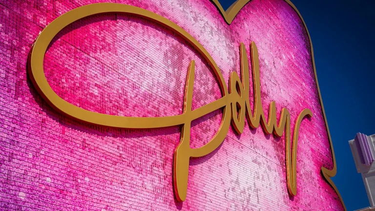 A large pink sequined heart sign with gold cursive lettering against a blue sky