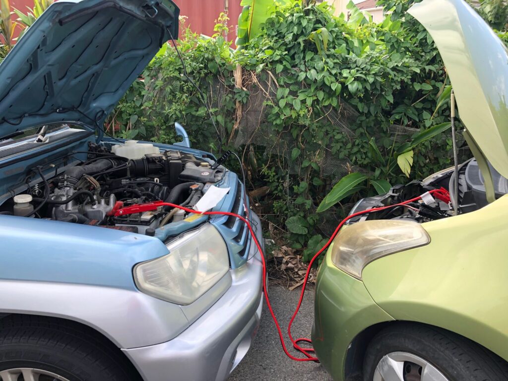 Two cars parked nose to nose with jumper cables running between their open hoods