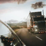 A semi truck driving on a highway under a warm orange sky