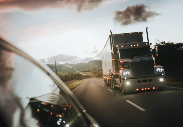 A semi truck driving on a highway under a warm orange sky