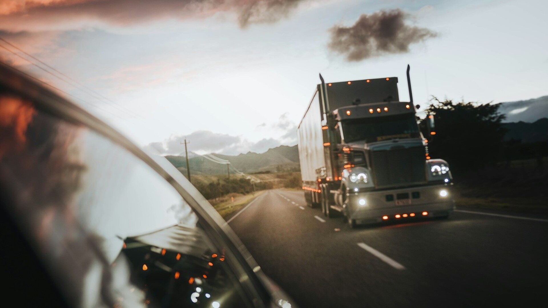 A semi truck driving on a highway under a warm orange sky