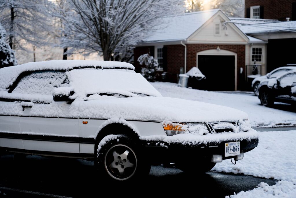 A white car covered in snow parked on a suburban street in winter