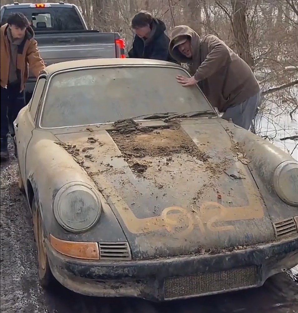 Dust-covered black 1969 Porsche with a 912 hood graphic being pushed out of a shed in the snow