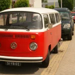 Red and white 1975 Volkswagen T2B bus parked at a curb (representative image)