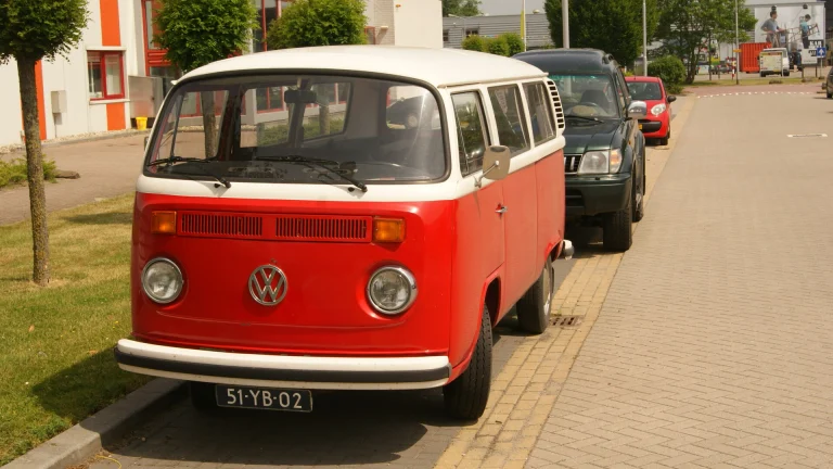 Red and white 1975 Volkswagen T2B bus parked at a curb (representative image)