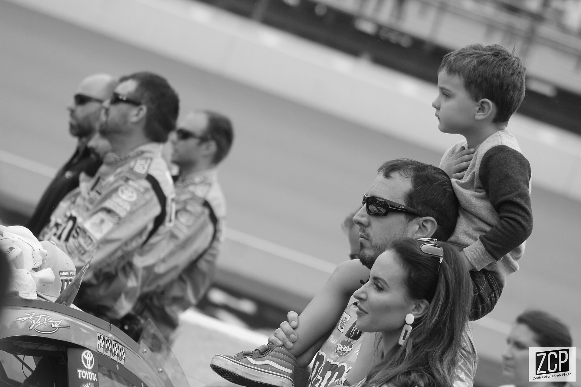 Young Brexton Busch sits on Kyle Busch's shoulders beside Samantha Busch at Michigan International Speedway in 2019