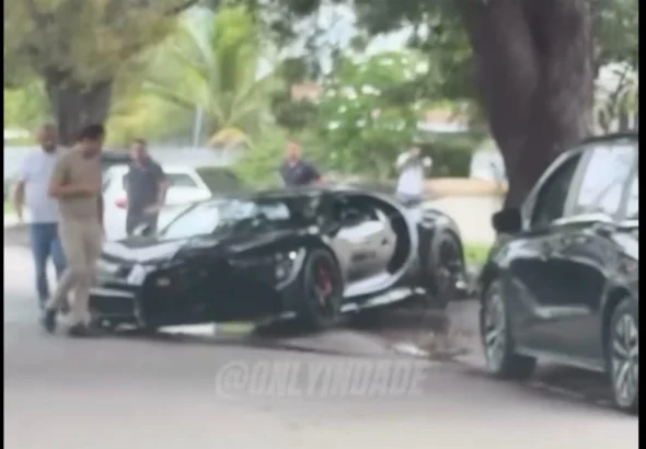 Black Bugatti Chiron with a crushed front end beside a curb and tree, from an @onlyindade Instagram reel