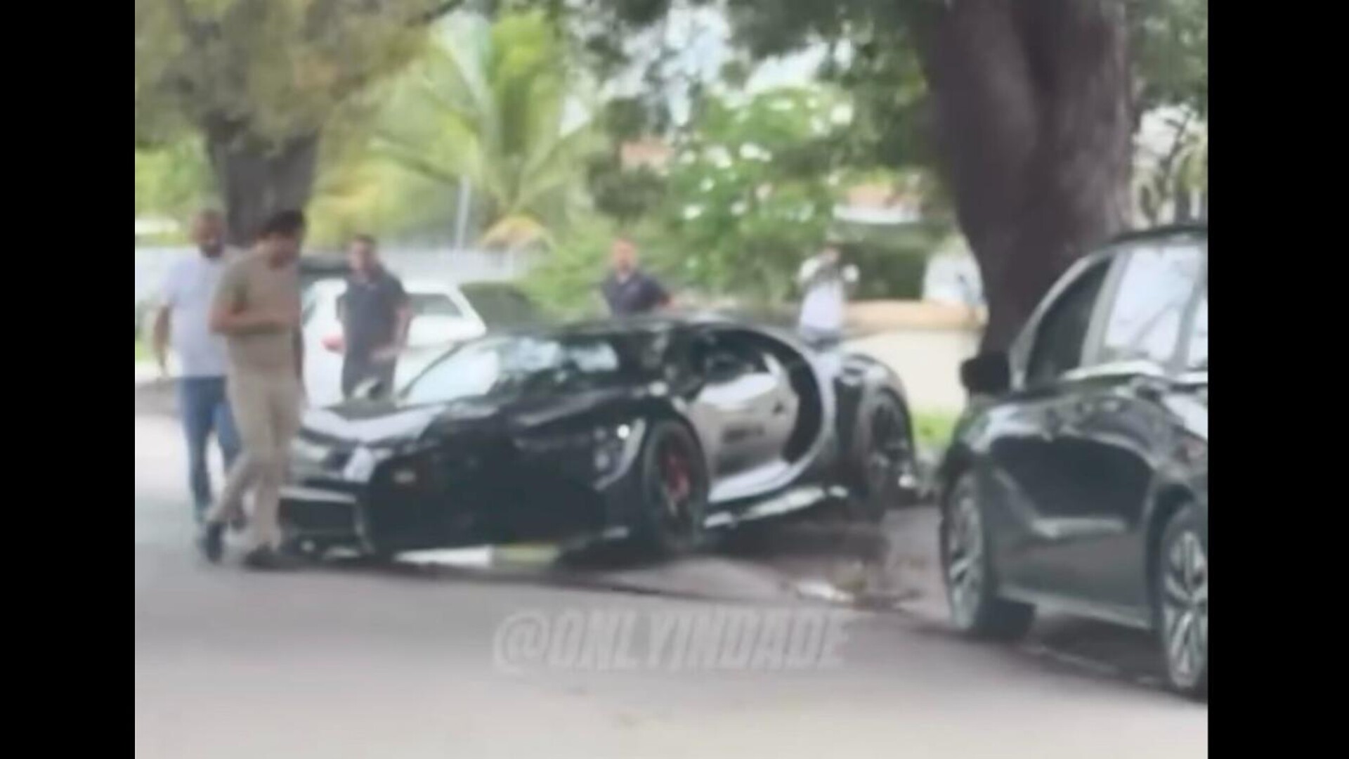 Black Bugatti Chiron with a crushed front end beside a curb and tree, from an @onlyindade Instagram reel