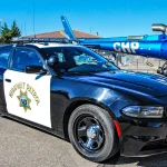 A black-and-white California Highway Patrol Dodge Charger patrol car parked in front of a CHP helicopter