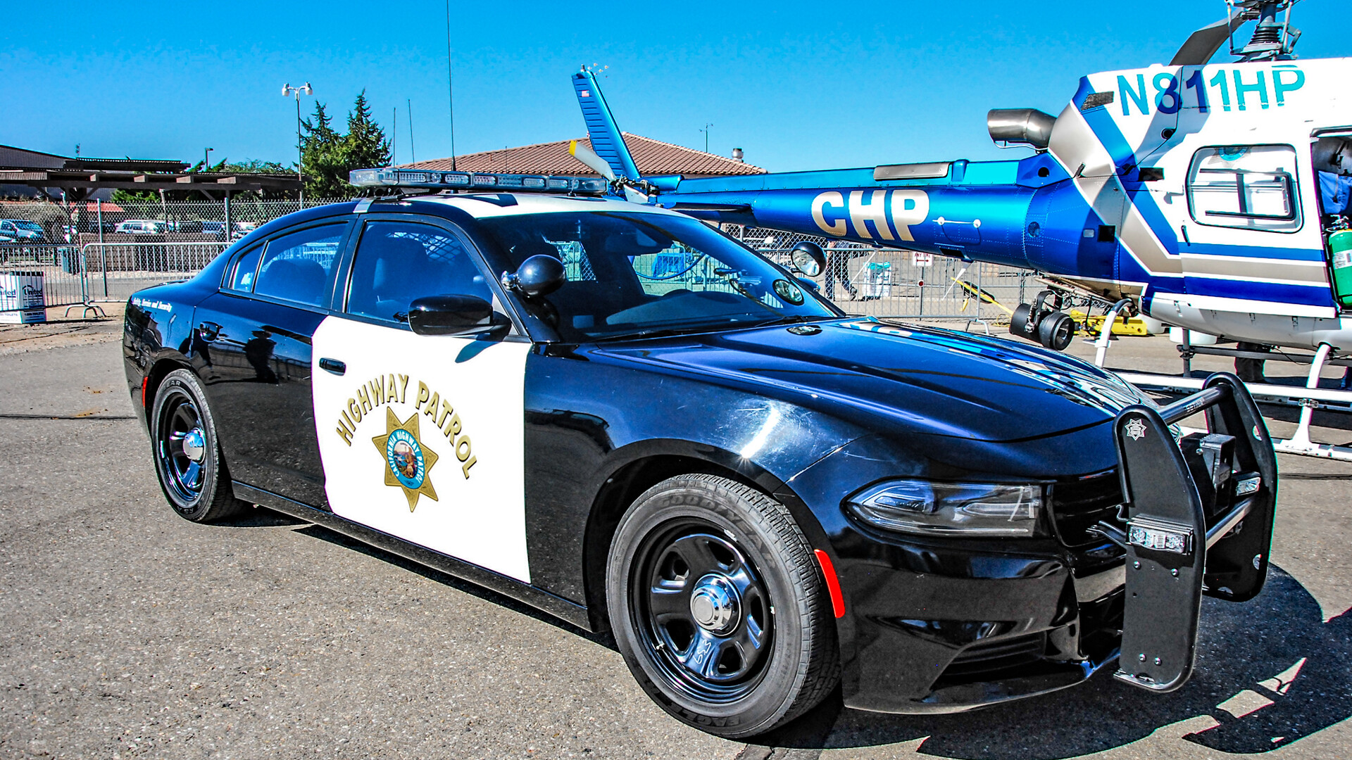 A black-and-white California Highway Patrol Dodge Charger patrol car parked in front of a CHP helicopter