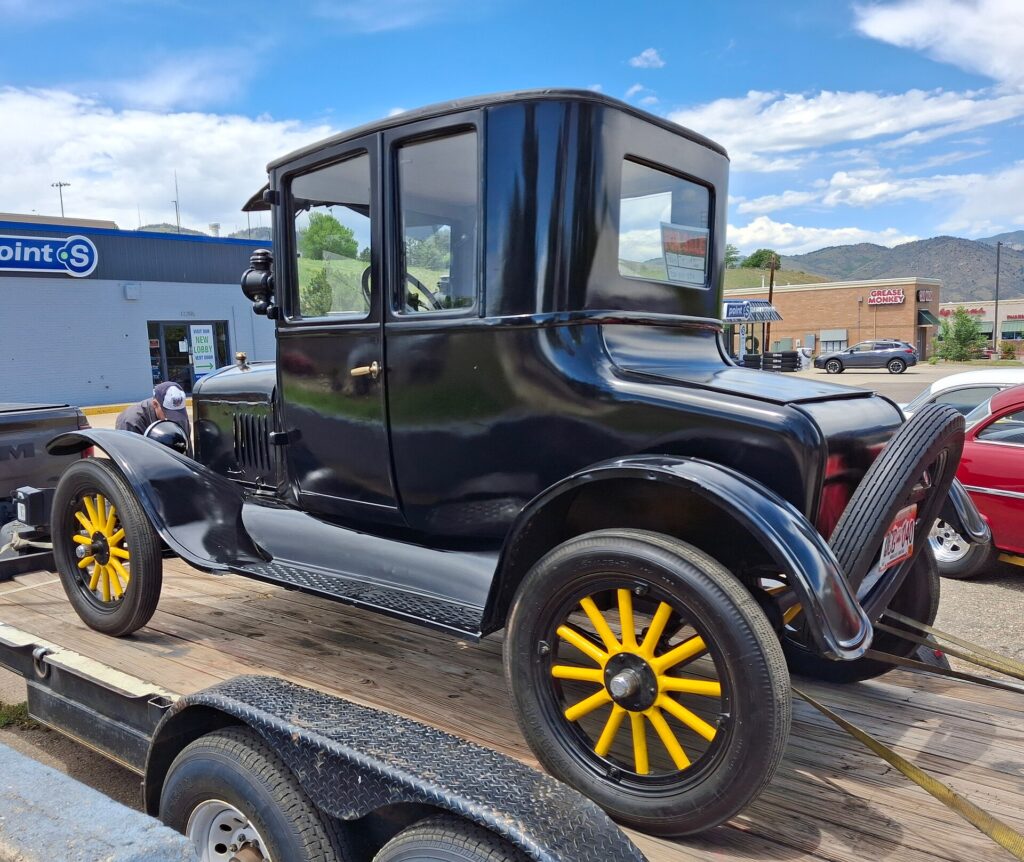 A black Ford Model T coupe strapped to an open flatbed trailer