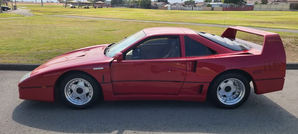 Side profile of the red Fiero-based Ferrari F40 kit car parked beside a grass field in Chula Vista