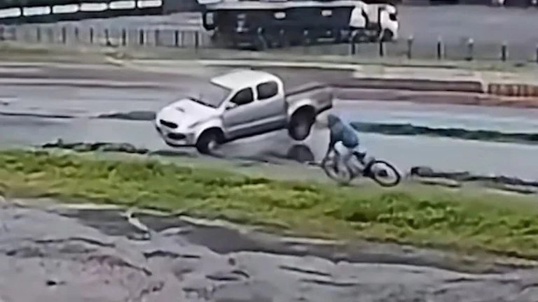 Surveillance video still of a silver Toyota Hilux pickup sliding toward a cyclist on a wet service road beside BR-163 in Marechal Cândido Rondon, Brazil