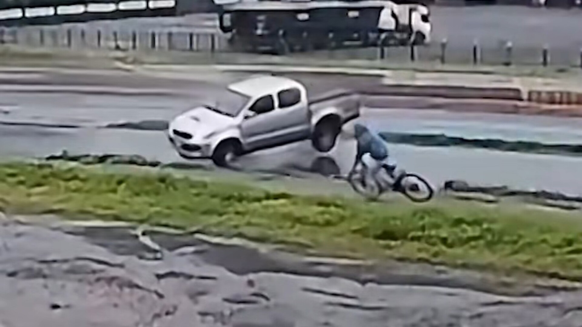 Surveillance video still of a silver Toyota Hilux pickup sliding toward a cyclist on a wet service road beside BR-163 in Marechal Cândido Rondon, Brazil
