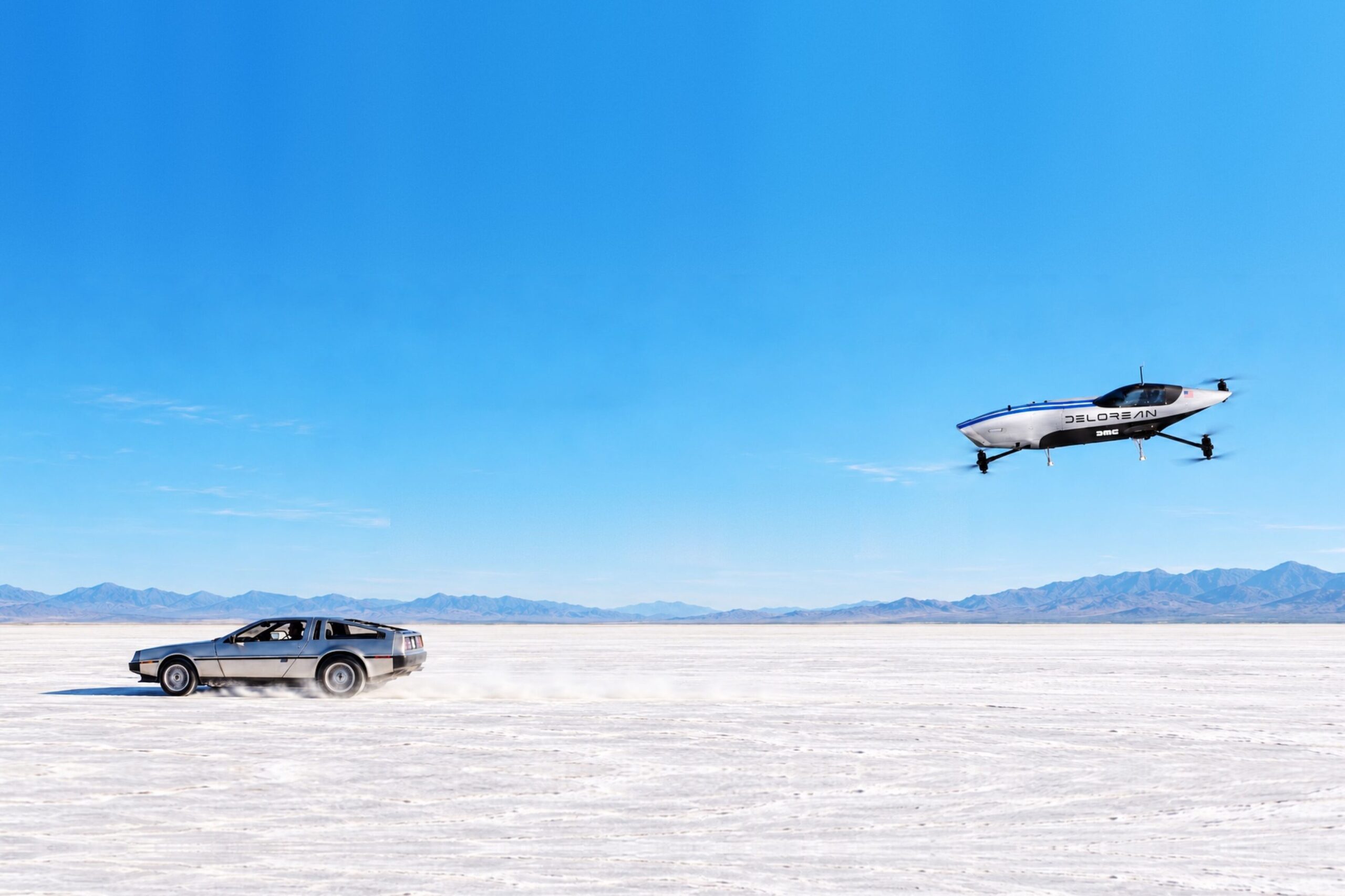 A silver Airspeeder aircraft in flight above a flat white plain as a DeLorean DMC-12 drives below it