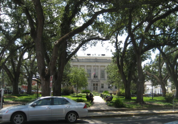 A silver sedan parked on Main Street in front of the Terrebonne Parish Courthouse in Houma, Louisiana, framed by live oak trees