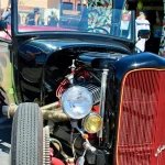 A black hot rod roadster with a red grille at a car show