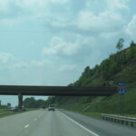 Interstate 64 westbound through a wooded hillside cut in West Virginia, with an I-64 shield sign