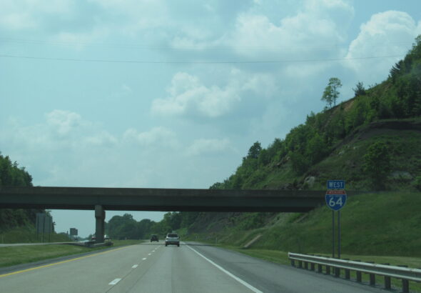Interstate 64 westbound through a wooded hillside cut in West Virginia, with an I-64 shield sign