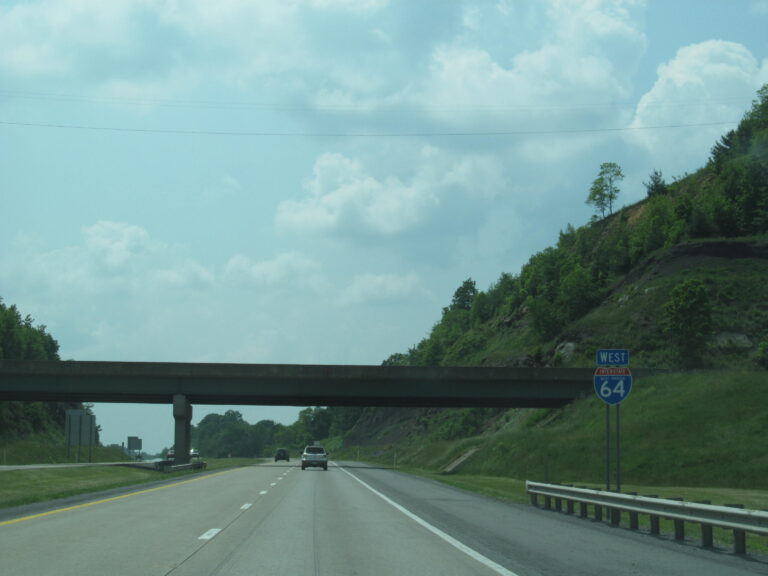 Interstate 64 westbound through a wooded hillside cut in West Virginia, with an I-64 shield sign