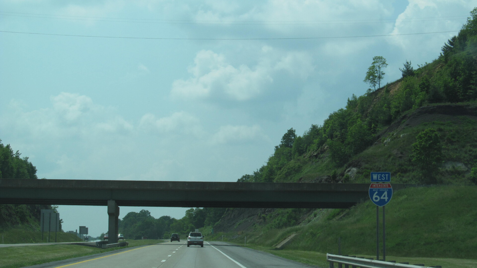 Interstate 64 westbound through a wooded hillside cut in West Virginia, with an I-64 shield sign