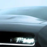 Sleek dark car with a bright, illuminated headlight