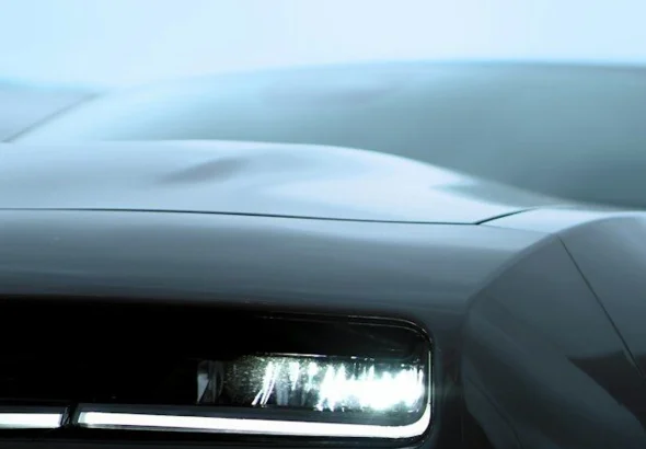 Sleek dark car with a bright, illuminated headlight