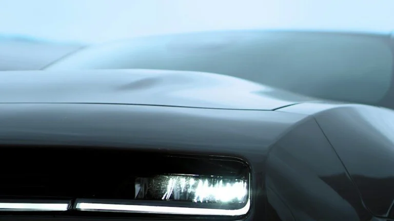 Sleek dark car with a bright, illuminated headlight