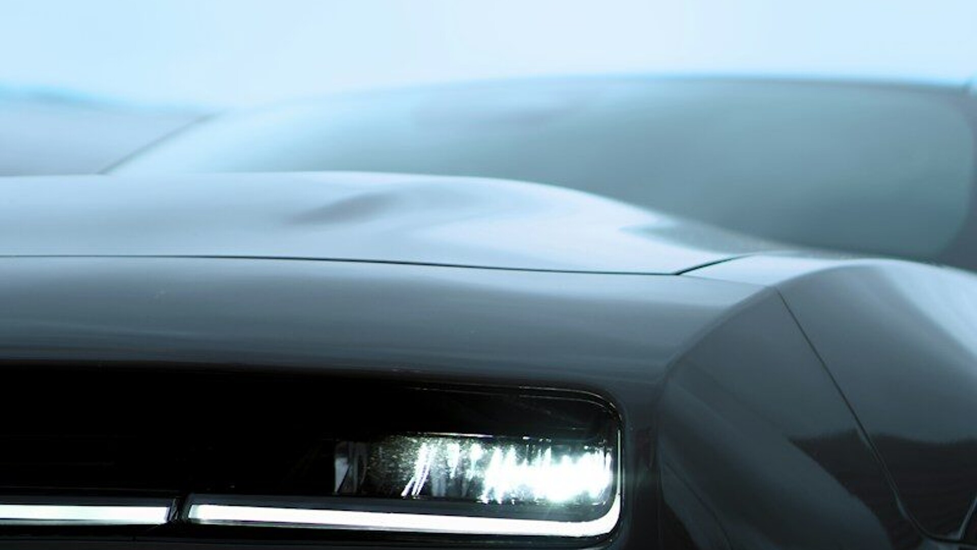 Sleek dark car with a bright, illuminated headlight
