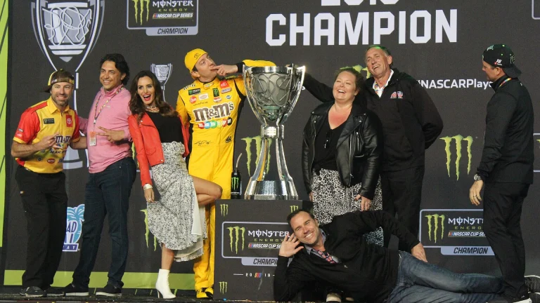 Kyle Busch in his yellow firesuit beside the trophy on the 2019 NASCAR Cup Series champion stage