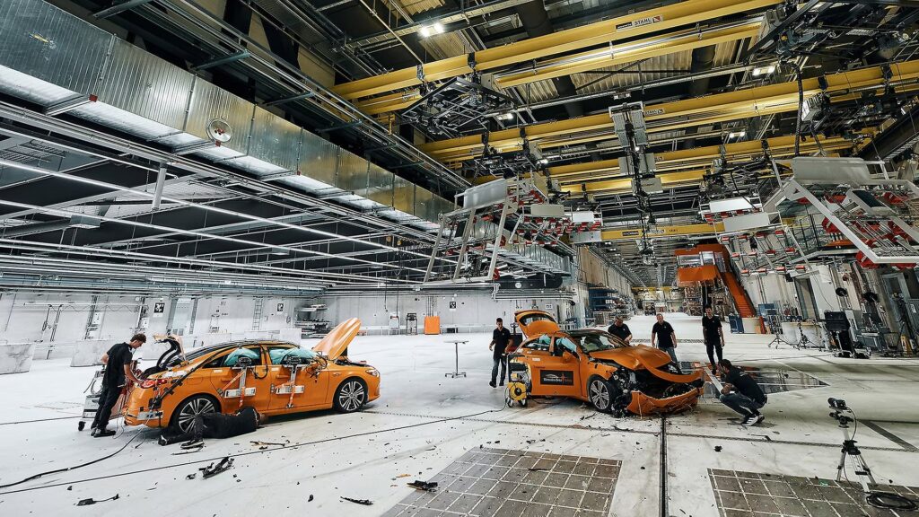 Engineers inspect two crashed Mercedes-Benz CLA test cars inside a crash test hall