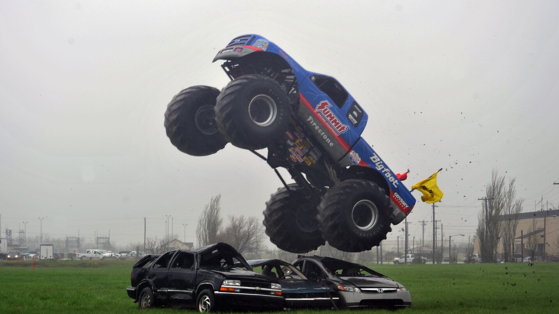 Blue Bigfoot monster truck landing on a row of junked cars