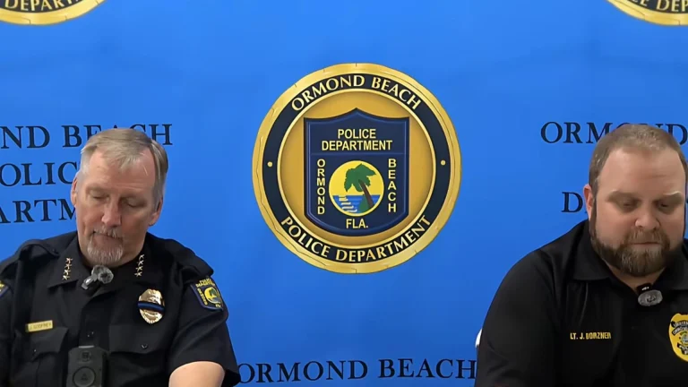 Two uniformed Ormond Beach Police Department officers seated in front of a department backdrop