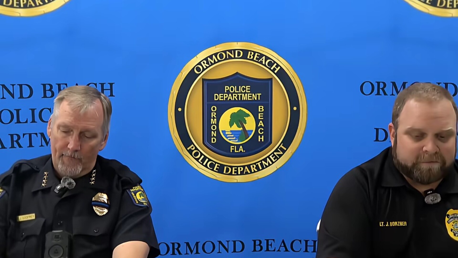 Two uniformed Ormond Beach Police Department officers seated in front of a department backdrop