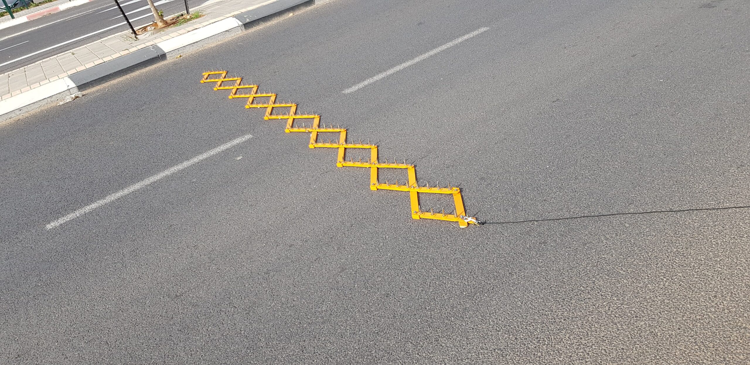 A yellow accordion-style police spike strip stretched across a traffic lane
